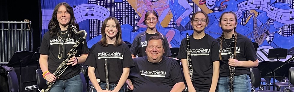 Teacher and students with wind instruments and wearing &#34;Darke County Band Directors Association&#34; shirts